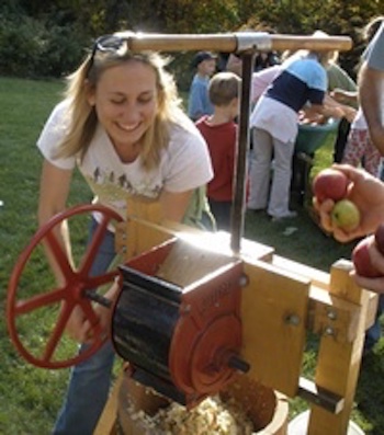 blonde woman cranking an apple cider press