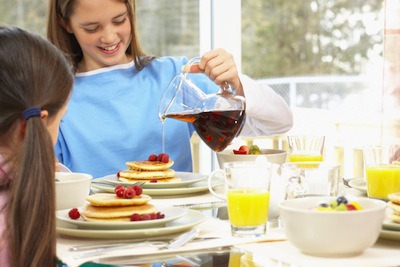 girl pouring maple syrup over pancakes at breakfast