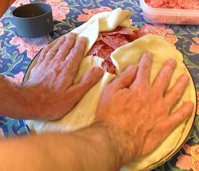 pressing down the dough on the top of a filled timpano