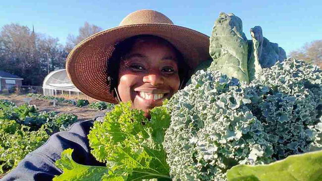Germaine Jenkins smiling while holding freshly harvested greens at Fresh Future Farm.