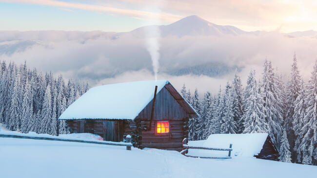 Fantastic winter landscape with wooden house in snowy mountains. Smoke comes from the chimney of snow covered hut. Christmas holiday and winter vacations concept