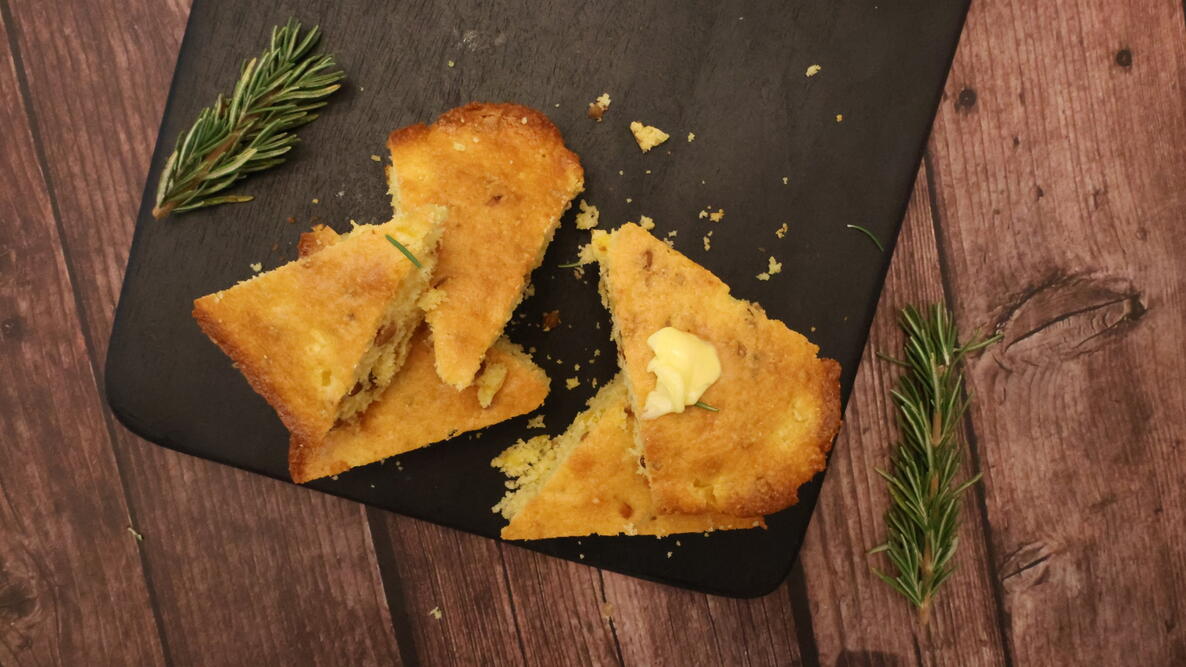 Corn Bread With Pine Nuts and Rosemary on a slate plate with a pat of butter on it
