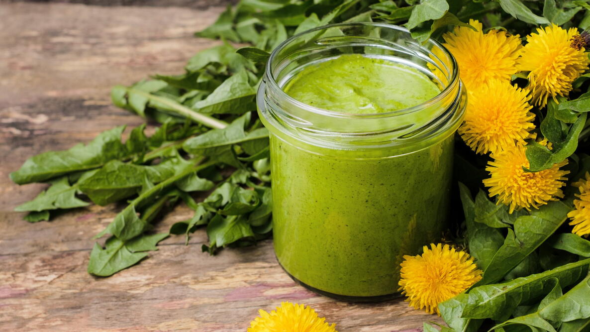 dandelion pesto in a jar on a table with dandelion flowers and greens