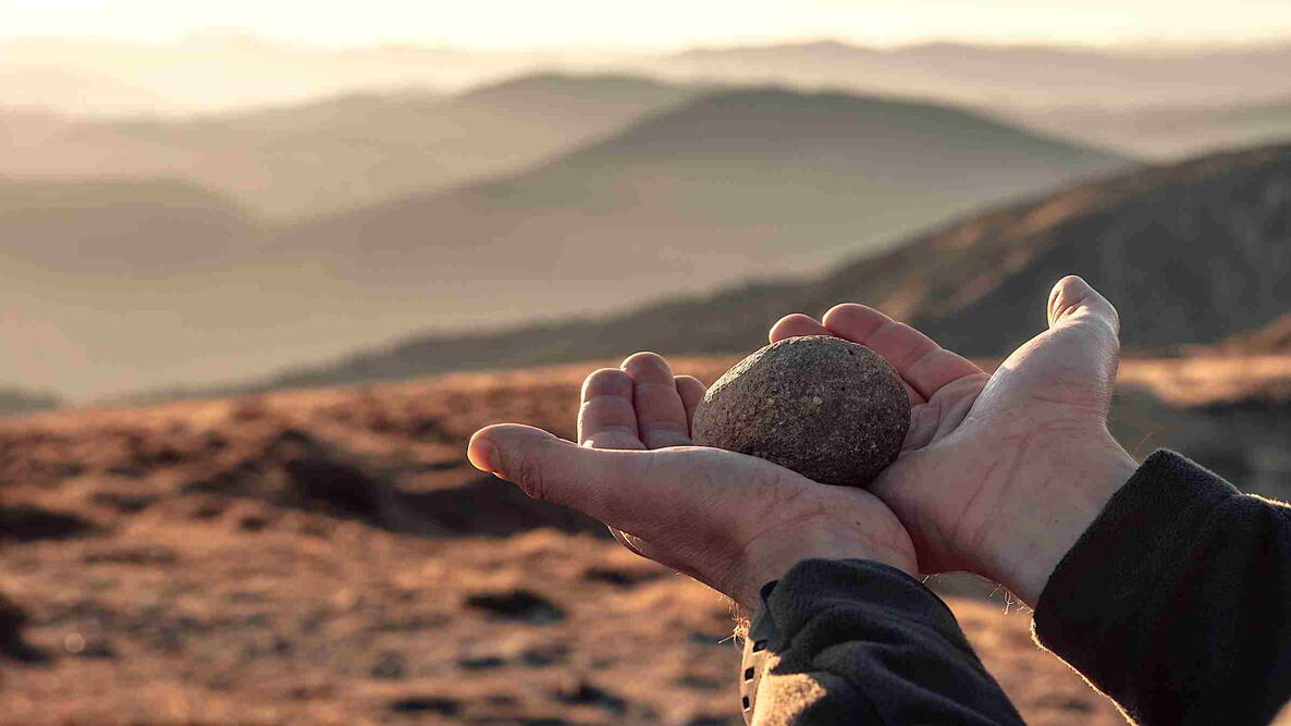 Hands holding a single smooth stone outdoors in soft, even light.