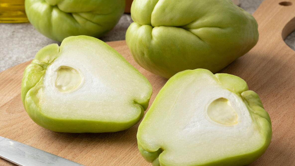 Whole and halved fresh chayote (Mirlitons) on a cutting board close up