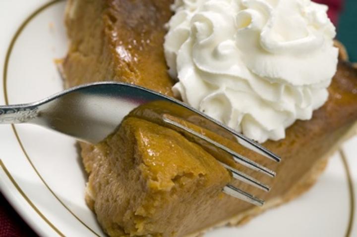pumpkin pie with whipped cream on top being cut into by a fork