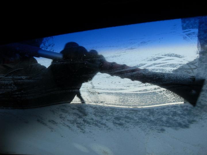 someone scrapping a frozen windshield in a winter storm